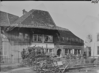 Doppelaufnahme, zweistöckiges Bauernhaus mit Querfirst über Tenntor, davor aufgestapeltes Brennholz, geziegeltes Satteldach Wohnbereich mit grossen Sprossenfenstern, davor eine Gruppe von Frauen und Mädchen an Bretterzaun