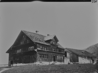 Vierstöckiges, gezimmertes Wohnhaus mit geknicktem Pultdach und Giebelbaube, giebel- und traufseitige Klebdächer, Butzen- und Sprossenfenster, Traufseite mittig Hauseingang, im Hintergrund gezimmerte Scheune mit Holzschalung