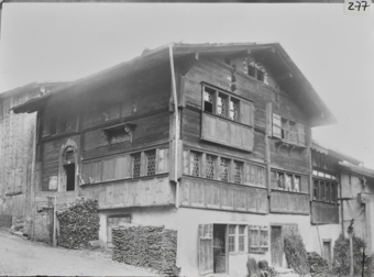 Vierstöckiges Wohnhaus an abfallender Strasse, Erdgeschoss gemauert, Oberbau geizmmert, Satteldach Butzenscheiben, an Hauswand  aufgestapeltes Brennholz