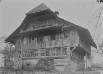 Dreistöckiges Wohnhaus, Fundament gemauert, oberen Etagen aus Holz, Krüppelwalmdach, aufgestapeltes Brennholz vor dem Haus, Holztreppe führt zum Hauseingang