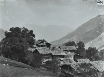 Ansicht eines Dorfes mit mehreren Häusern mit Satteldächern, Häuser mehrheitlich aus Holz, Gelände abfallend, mehrere Bäume rund um das Dorf, im Hintergrund Bergkette