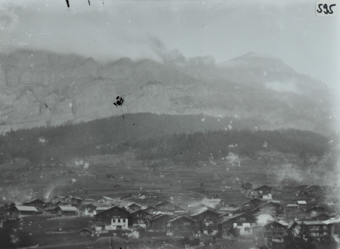 Ansicht des Dorfes aus der Vogelperspektive, mehrere Gebäude ersichtlich, insbesondere aus Holz und mit Satteldächern, Hügel resp. Gebirge im Hintergrund