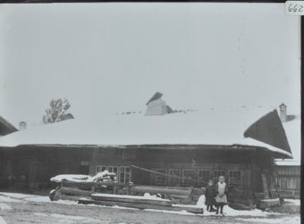 Zweistöckiges Bauernhaus aus Mischbau, Fusswalmdach, vor dem Haus liegt Holz, zwei Kinder posieren vor dem Haus, Umgebung verschneit