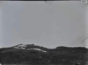 Ansicht einer hügeligen Landschaft mit diversen Gebäuden und Bäumen, Hügelspitze verschneit