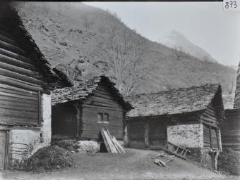 Ansicht eines Dorfteils mit mehreren Gebäuden aus Holz und Fundament aus Stein, Gebäude einstöckig, Satteldächer, Weg verbindet die Häuser, Berg im Hintergrund