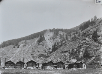 Ansicht des Bergdorfes mit mehreren Häusern, Häuser aus Holz mit gemauerten Fundament, Satteldächer, steiler steiniger Hang hinter dem Dorf