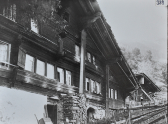 Mehrstöckiges Bauernhaus mit Wänden aus Holz, gemauertes Fundament, Schleppdach, gestapeltes Brenholz vor dem Haus, Holzzaun führt vor dem Haus vorbei