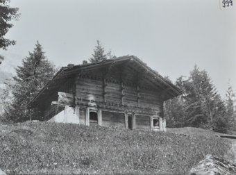 Scheune mit Wänden aus Holz, Fundament aus Stein, Satteldach, Dach mit Steinen verstärkt, Scheune am Hang erbaut, im Hintergrund Bäume und Tannen