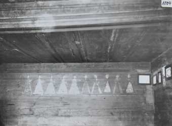 Innenaufnahme eines Zimmers, die Wände sind verziert mit Bildern, weitere Bilder hängen an den Wänden, Decke aus Holz 