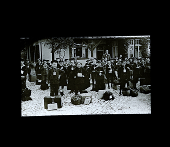 Kindergruppe mit umgehängten Kartonschildern und Reisegepäck, darunter der «Hausvater»