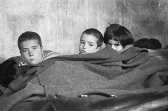 Drei Kinder im Bett liegend in einer Baracke