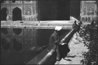 Persien, Isfahan: Palast der 40 Säulen (Lokalisierung unsicher); Menschen sitzen auf kleiner Mauer, welche einen Teich umgibt, im Hintergrund Gebäude