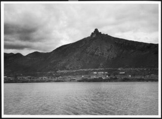 Russland, Nordossetien: Siedlung (Lokalisierung unsicher); Siedlung am Wasser, dahinter Berg mit einer Festung