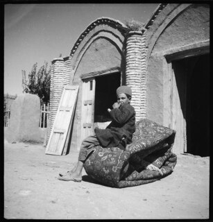 Persien: Knabe; Ein Knabe sitzt auf einem gerollten Teppich vor einem Gebäude, aufgenommen auf der Fahrt nach Isfahan