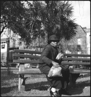 USA, Savannah/GA: Menschen; Eine Frau sitzt auf einer Bank, im Hintergrund Häuser