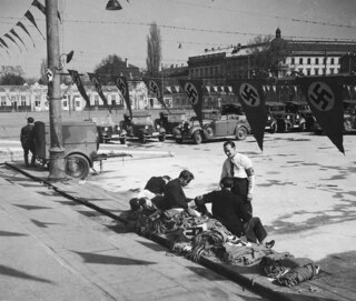 Österreich, Wien: Menschen; Junge Männer, die auf einem Stoss Hakenkreuzflaggen sitzen, im Hintergrund Armeefahrzeuge