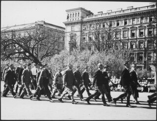 Österreich, Wien: Menschen; Männer maschieren durch die Strassen

Im Hintergrund das Haus Schillerplatz 4.