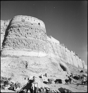 Afghanistan, Ghazni (Ghazna): Stadtansicht; Ein runder Turm in einer Mauer, am Fuss der Mauer Männer und Frauen mit Dromedaren und Maultieren