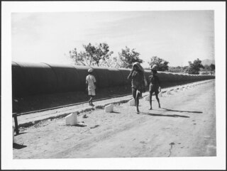 Britisch-Indien, Bombay (Mumbai): Landschaft; Rohre neben einer Strasse, davor Menschen