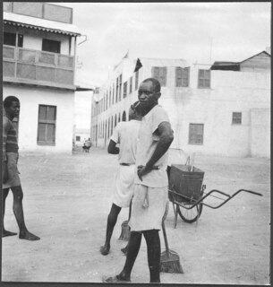 Italienisch-Ostafrika, Massana (Massawa, Massaua): Hafen; Drei Männer mit einer Schubkarre und Besen vor Gebäuden auf einem Platz