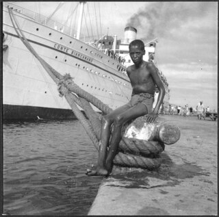 Italienisch-Ostafrika, Massana (Massawa, Massaua): Hafen; Ein Knabe sitzend auf einem Poller, an den die Conte Biancamano angeleint ist