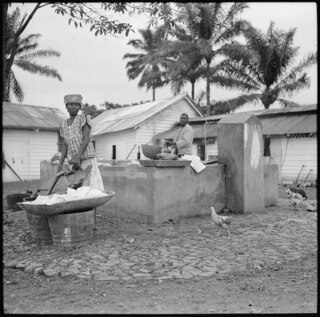Portugal, San Thomé (São Tomé und Príncipe): Menschen; Frau und Mann waschen am Brunnen Kleider, umgeben von einzelnen Hühnern