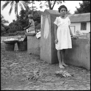 Portugal, San Thomé (São Tomé und Príncipe): Menschen; Ein farbiges Kind steht am Brunnen; Frau im Hintergrund am waschen