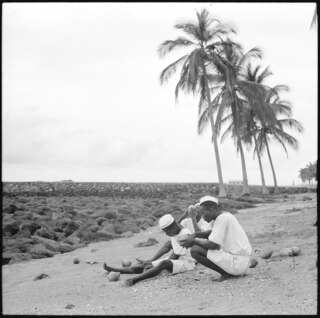 Portugal, San Thomé (São Tomé und Príncipe): Menschen; Farbige Matrosen sitzend, am Boden am Brotbaumfrüchte essen; Palmengruppe im Hintergrund