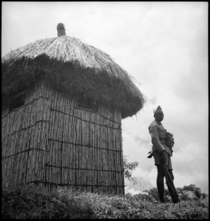 Belgisch-Kongo, Adranga: Garnison; Soldat steht neben einer Strohhütte auf einer Anhöhe
