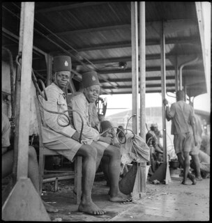 Belgisch-Kongo, Fluss Kongo: Soldaten; Mehrere farbige belgische Kolonialsoldaten sitzen in Uniform, aber barfüssig auf einer Holzbank auf dem Schiff