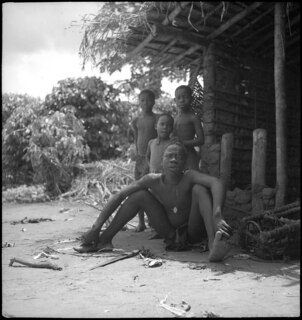 Belgisch-Kongo, Molanda (Malanda): Menschen; Eine Gruppe von nackten Kindern, teilweise sitzend am Boden neben Sträuchern und einer Hütte