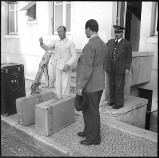 Portugal, Estoril: Menschen; Herr Bossi steht abgewendet mit zwei weiteren Personen neben mehreren Reisekoffern vor einem Gebäude