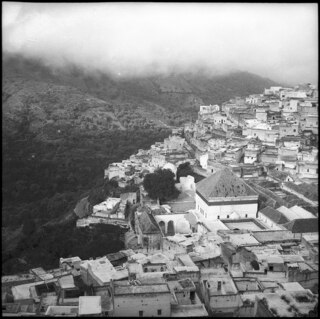 Französisch-Marokko, Moulay Idriss: Dorfansicht; Sicht auf Moulay Idriss von erhöhter Lage mit Blick auf Mausoleum und Minarett und wolkenverhangene Hügellandschaft