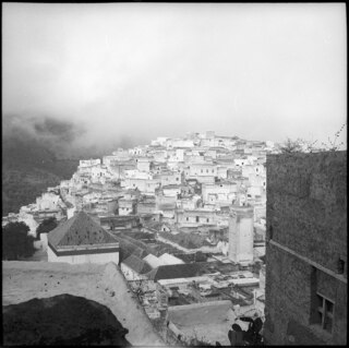 Französisch-Marokko, Moulay Idriss: Dorfansicht; Sicht auf Moulay Idriss von erhöhter Lage mit Blick auf Mausoleum und Minarett und wolkenverhangene Hügellandschaft