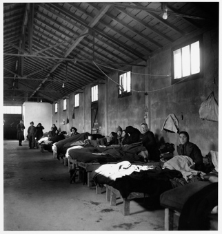 Winterlich gekleidete Lagerbewohnerinnen auf Betten sitzend in einer Baracke des Internierungslagers Rivesaltes