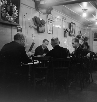 Männerrunde am Jassen in Wirtshaus der Altstadt. An der Wand diverse Hüte, Werbeplakat St. Moritz von 1934, in einem Holzkasten Kranz und Medaillen eines Sportvereins
