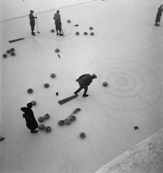 5 Curlingspieler , Curlingsteine und Besen auf Eisfeld.  Aufnahme von oben (Zuschauertribune)