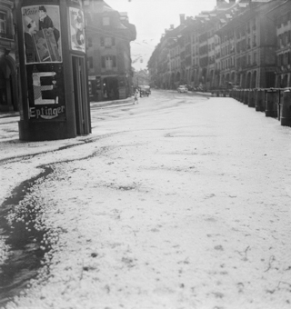 Gerechtigkeitsgasse mit Hagel infolge Hagelunwetter vom 23.5.1950. Plakatsäule und Pissoir an der Nydegggasse, Plakat «Zirkus Knie» von 1950, Plakat «Eptinger Mineralwasser». Rechts die Poller oberhalb Nydeggstalden