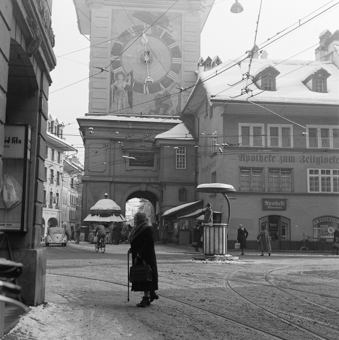 Theaterplatz mit Zeitglockenturm, Kiosk, Apotheke zum Zeitglocken, links Marktgasse 2 mit Schaukasten von «Schmid fils Fourrures». Auf der Kreuzung Verkehrskanzel mit Verkehrspolizist, Passanten, Auto (VW Käfer), Fahrrad