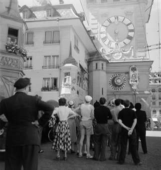 Leute in sommerlicher Kleidung beim Besichtigen des Zeitglockenturms. Zwei Erker an der Ecke Kramgasse/Hotelgasse. Haus der Drogerie zum Zeitglocken (Scheidegger) mit Fresko an der Fassade 