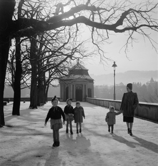 Frau in Pelzjacke und Turban mit 4 Kindern in Winterkleidern auf der verschneiten Münsterplattform. Pavillon, Kandelaber