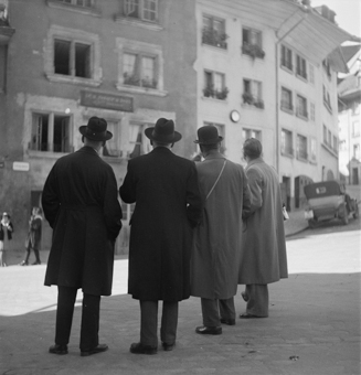 Haus Nydeggstalden 1 mit Einschussloch vom «Stäcklichrieg» 1802. Davor vier Männer mit Mänteln und Hüten beim Betrachten des Hauses. Rechts Nydeggstalden mit parkiertem Auto