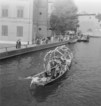 Matte-Chilbi im Mattenquartier- Festlich geschmücktes Boot im Mattekanal, mehrere Bootspassagiere (sommerlich gekleidete Kinder und Erwachsene), zwei Bootsführer mit Rudern. Bootssteg beim Matteschulhaus, Zuschauer und Spaziergänger. Mit Lämpchen geschmückte Uferpromenade entlang dem Kanal