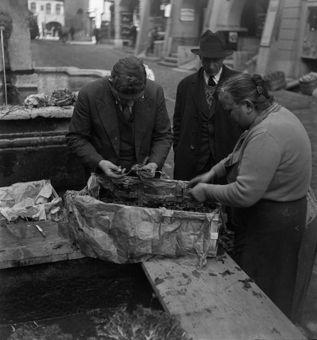 Marktleute beim Anna Seiler-Brunnen am Gemüsewaschen. Ein Passant in Mantel und Hut schaut zu