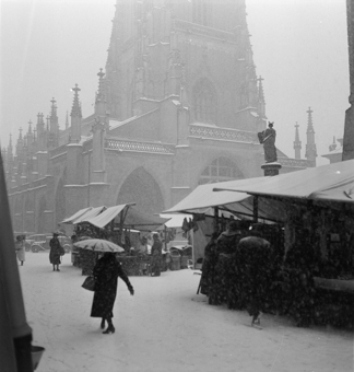 Fleischmarkt auf dem Münsterplatz bei Schneefall. Marktstände mit Holzgerüsten und Dächern. Marktbesucher mit Schirmen. Brunnenfigur vom Mosesbrunnen, Münster, verschneiter Münsterplatz. 