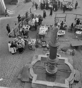 Fleischmarkt auf dem Münsterplatz, Marktstände, Fleisch und Würste an Haken und auf Verkaufstheken, Körbe, eine «Hutte», Leiterwagen. Fleischhändler in weissen Schürzen. Im Vordergrund der Mosesbrunnen.  Aufnahme aus Haus am Münsterplatz