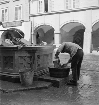 Mann in Arbeitskleidung reinigt Holzkisten im Simson-Brunnen,  Holz-Zeine und Zinnkessel. Hinten Laubengänge von Kramgasse 40 mit Firmenschild  «A. Steiger, Elektr. Anlagen», und Haus Nr 36 mit Tor (heute Konservatorium für Musik)