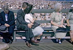 Menschen auf  Bank sitzend, daneben zahlreiche Menschen am Strand und im Wasser