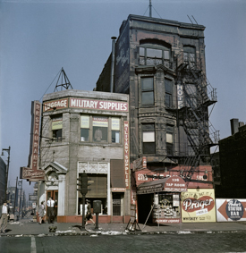 Warenhaus mit Aufschrift "Luggage, Military Supplies", daneben Haus mit Hotel und Getränkeladen