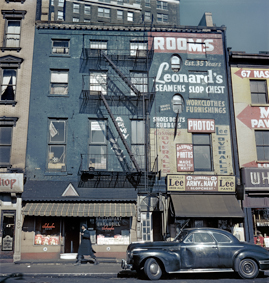 Gebäude mit Aufschrift «Rooms, Leonard's Seamens Slop Chest» (Zimmer und Laden für Seeleute), unten Restaurant Schaefer, am Haus Balkone und Feuerleitern, vorne ein Auto